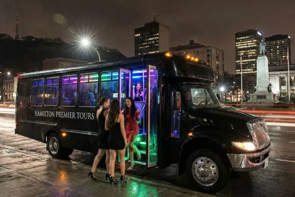 Luxury party bus rental Hamilton with LED lighting and group boarding at night.